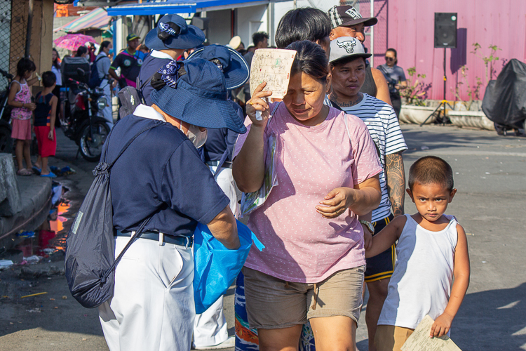 A beneficiary waits with her child as they line up for the distribution of the GI sheets. 【Photo by Marella Saldonido】