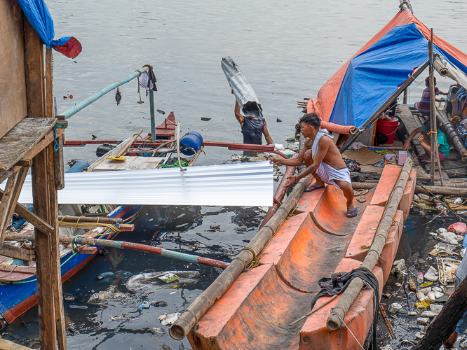 Despite the challenge in transporting the GI sheets over the water, Isla Puting Bato residents work hard in rebuilding their homes. 【Photo by Jeaneal Dando】