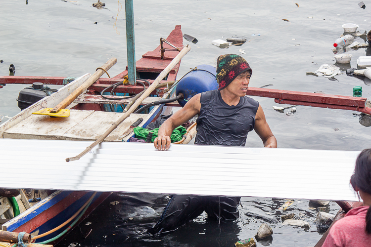 An Isla Puting Bato resident perseveres in transporting the GI sheets over the water. 【Photo by Marella Saldonido】