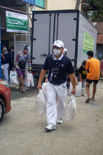 A volunteer helps a beneficiary carry his two 10-kg sacks of rice. 【Photo by Matt Serrano】