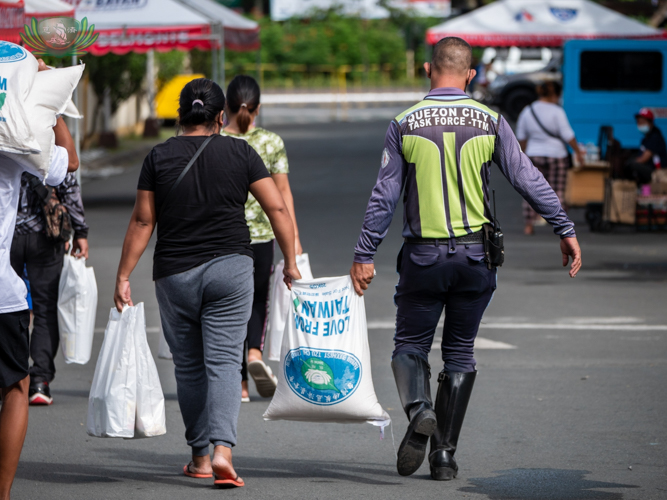 A beneficiary gets help carrying her rice relief from a member of the Quezon City Task Force for Transport and Traffic Management.  【Photo by Daniel Lazar】