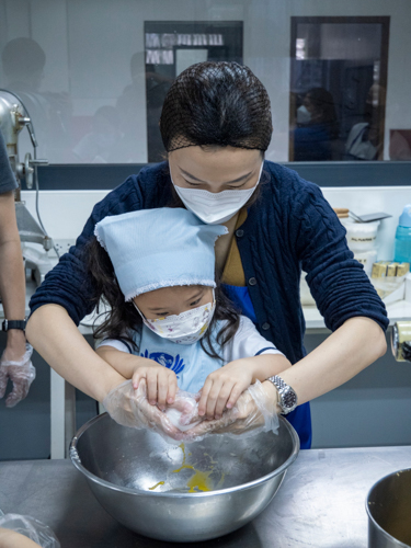 Ensuring moisture and flavor to the cookies, a parent guides her daughter in beating eggs into the creamed butter and sugar, one at a time. 