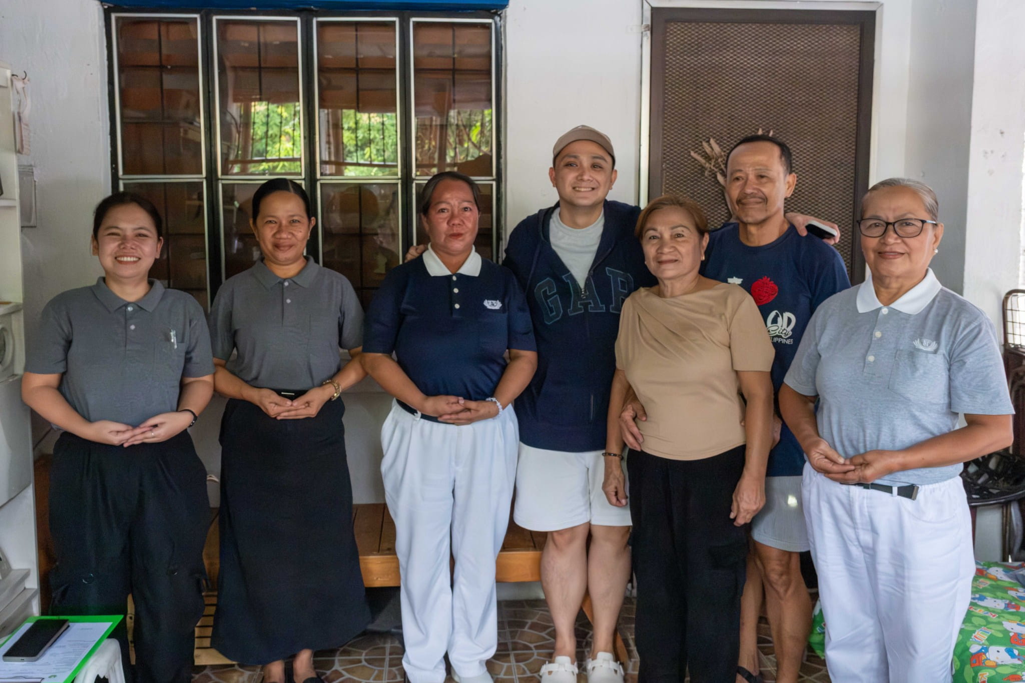 (From left) Tzu Chi Charity Department Social Welfare Officer Jackie Raper and Social Service Officer Julie Collado, and Tzu Chi volunteers Esperanza Celon (in blue) and Emma del Rosario (in light gray) visit medical assistance beneficiary Steven Nico Flores and his parents Roselyn and Fernando (fourth, fifth, and sixth from left) in their home in Bacoor, Cavite, more than a year after his heart surgery.