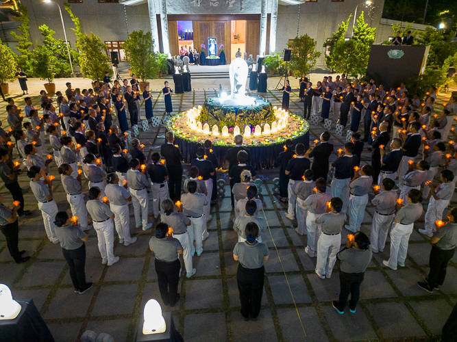 As dusk turns into night, the Buddha Bathing Ceremony draws to a close with Tzu Chi volunteers raising their lotus flower lights before the centerpiece inspired by a pilgrimage to Vulture Peak.