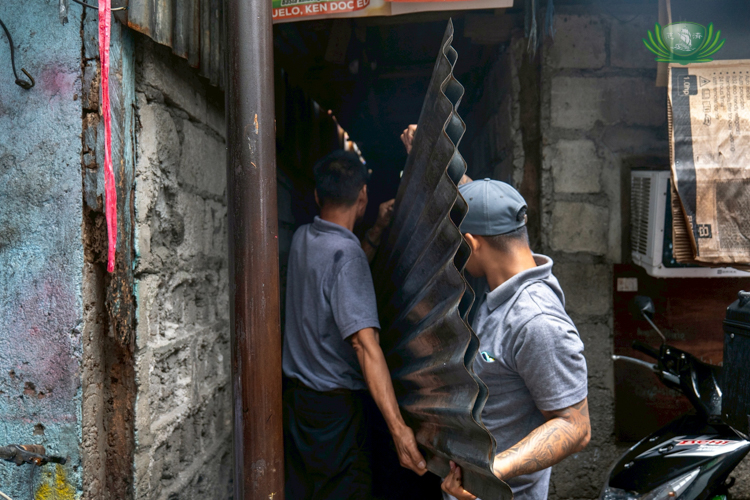 Tzu Chi staffers squeeze into a dark and narrow alley in Samson Road, Caloocan, to deliver GI sheets and other provisions to medical assistance beneficiary Reynalda Francisco.