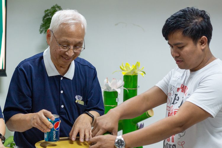 Tzu Chi volunteer James Cheng assists TechVoc alumni as they turn over the contents of their coin bank. The donated money will be pooled together to help future batches of TechVoc scholars.