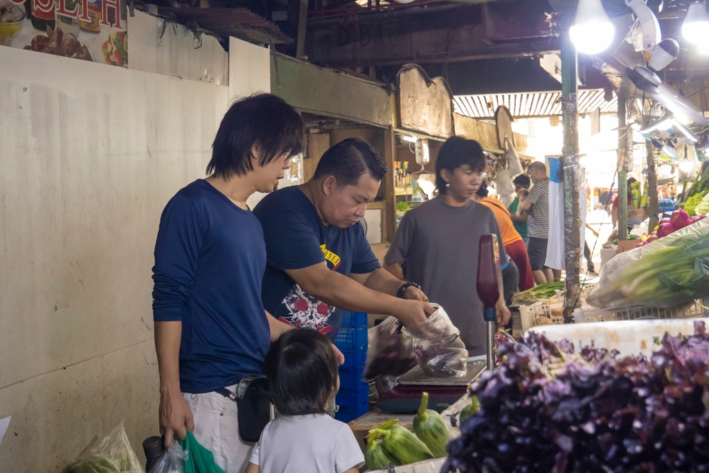 Allan Anggala (left, in blue), takes the lead in buying vegetables before teaching his son Ava some valuable tips to make a good purchase.