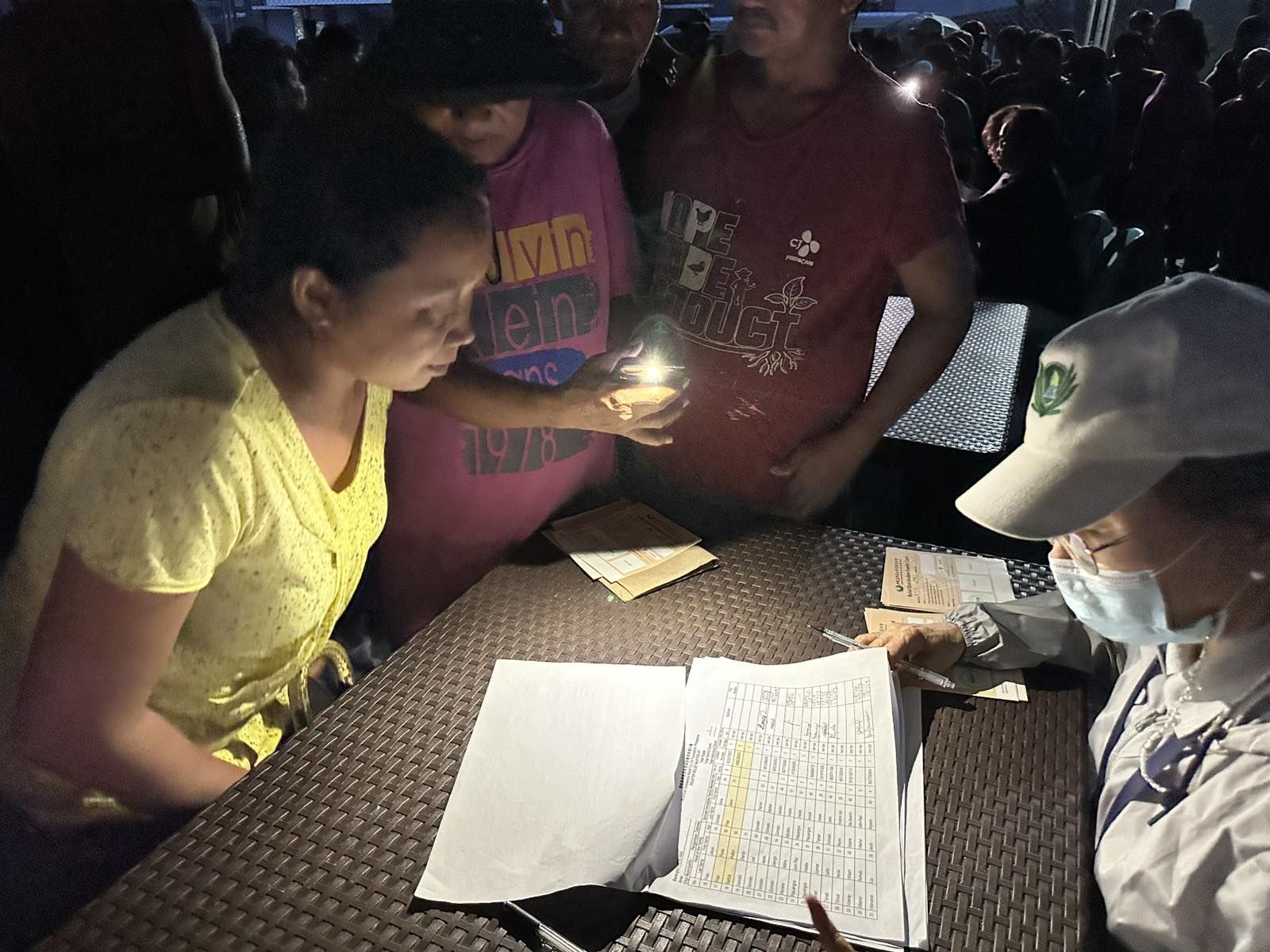 A Tzu Chi volunteer checks her list for the name of a Panganiban resident while a man uses his cellphone flashlight to help. 