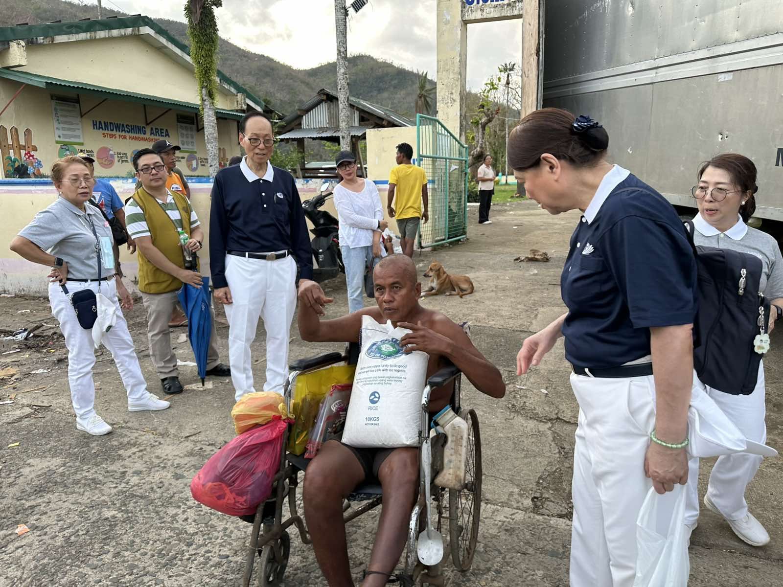 Tzu Chi Bicol head volunteer Antonio “Tony” Tan and his wife Therese (in blue) chat with a beneficiary in a wheelchair after he receives his 10-kg sack of rice. 