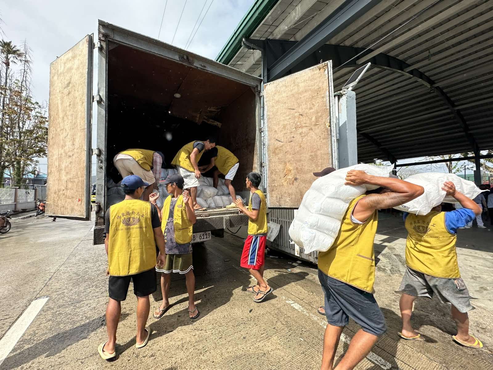 Happy volunteers in Panganiban transfer sacks of rice from a truck to the covered court. 