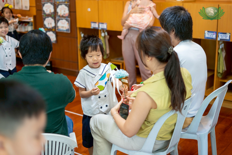 A student presents his gifts of gratitude to his parents, a handmade paper necktie and a flower.