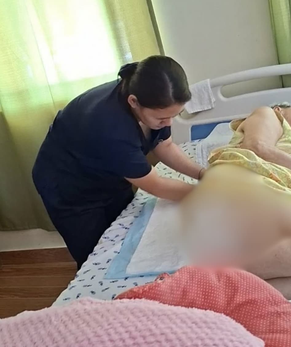 Carefully attending to her patient's needs, Renancie Abiera takes diligent care of an  elderly woman.