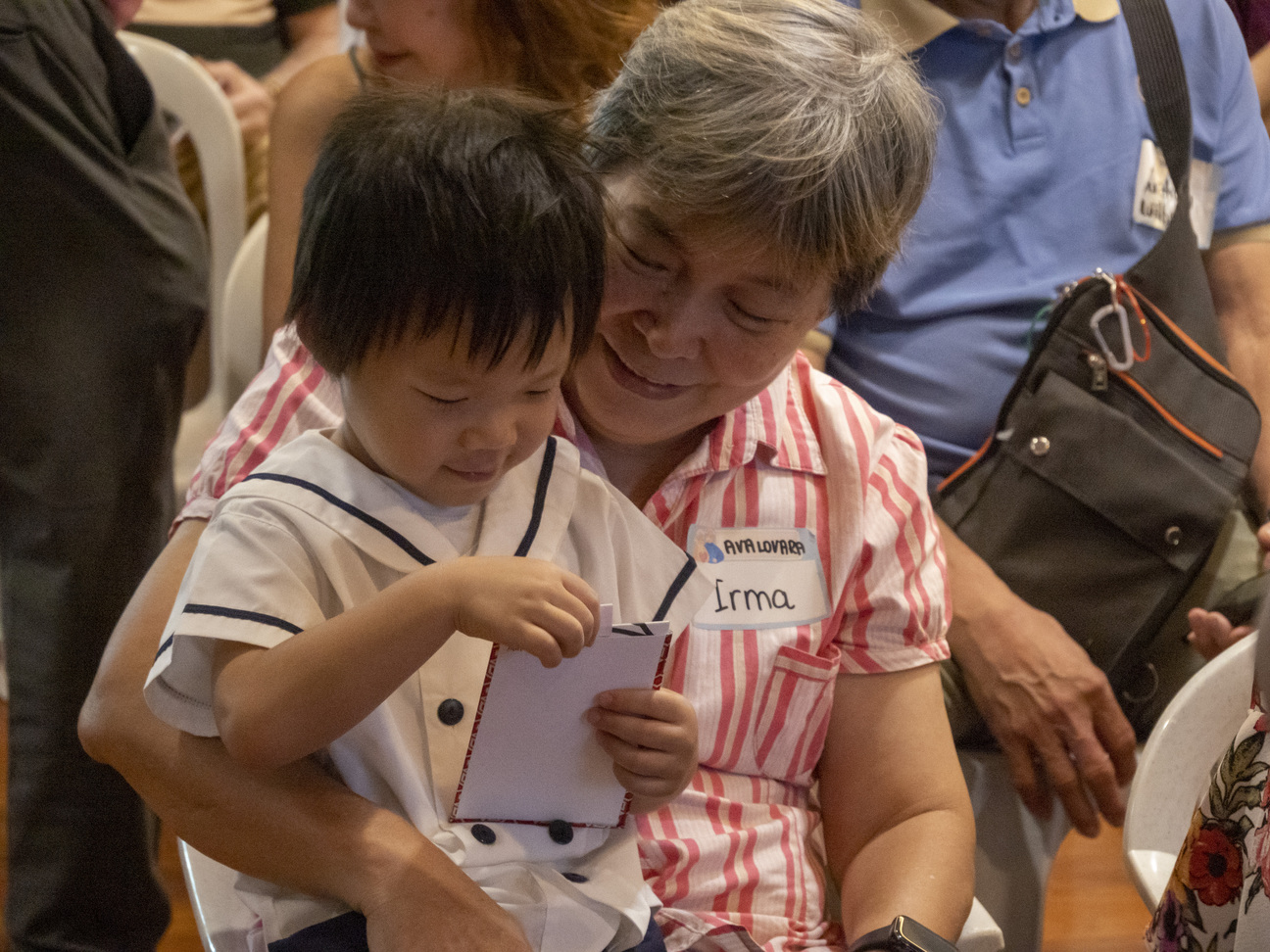 A young preschooler happily shows his artwork to his grandparent.