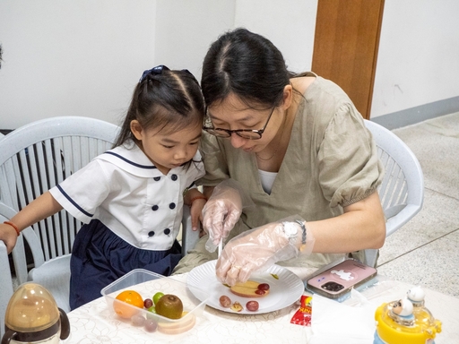 A parent guides her daughter in making the fruit art.