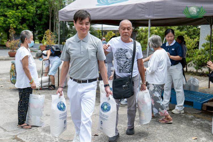 Tzu Chi volunteer Ken Chua (in gray) assists a medical assistance beneficiary with his sacks of rice.