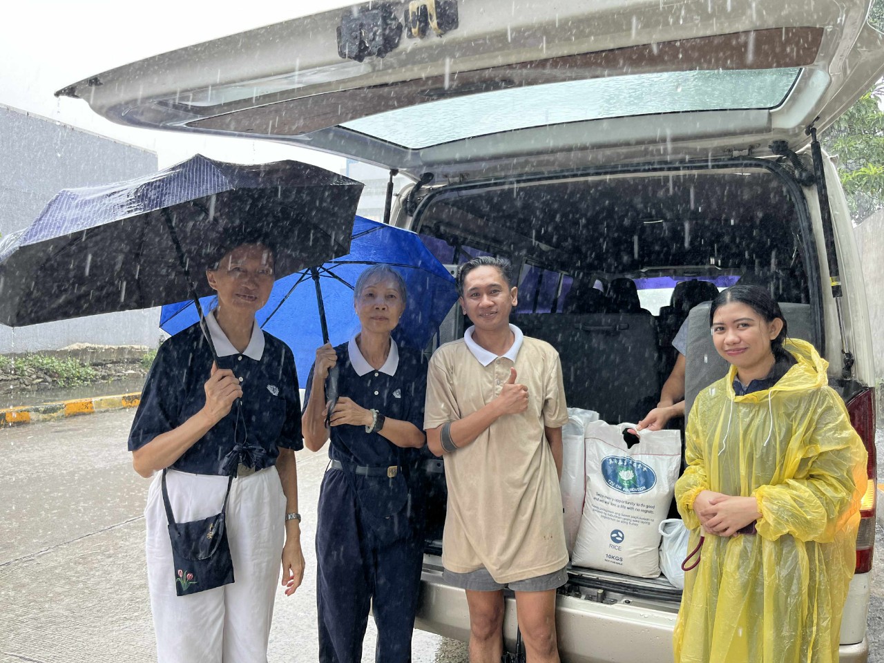 Even in a downpour, relief distribution continues. Marco Caumeran (third from left), a Tech-Voc (caregiving) scholar, received basic provisions and construction materials from volunteers. 