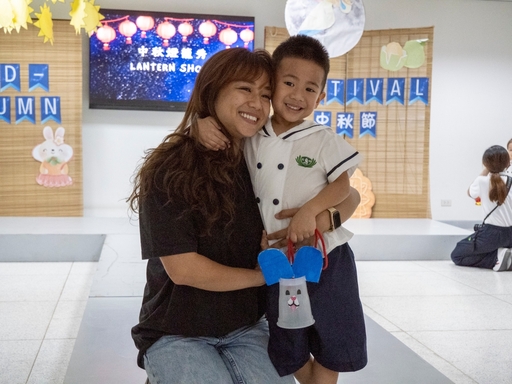 A parent happily poses with her son while showing the lantern they made.