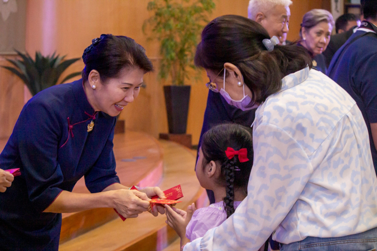 Bliss radiates as Tzu Chi Philippines Deputy CEO Woon Ng presents an angpao to a young attendee, her mother watching the heartwarming exchange with gratitude.