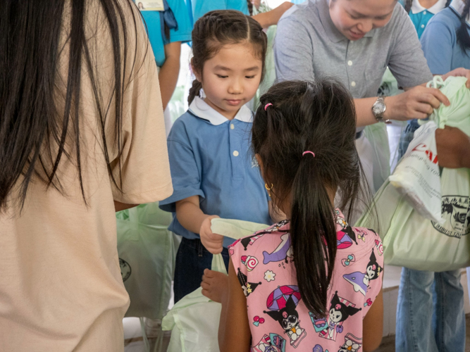 A young volunteer gives a bag of school supplies to a student.