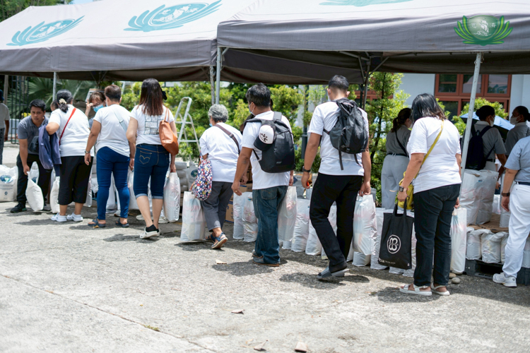 Medical assistance beneficiaries form an orderly line to claim their bags of rice and assorted groceries.