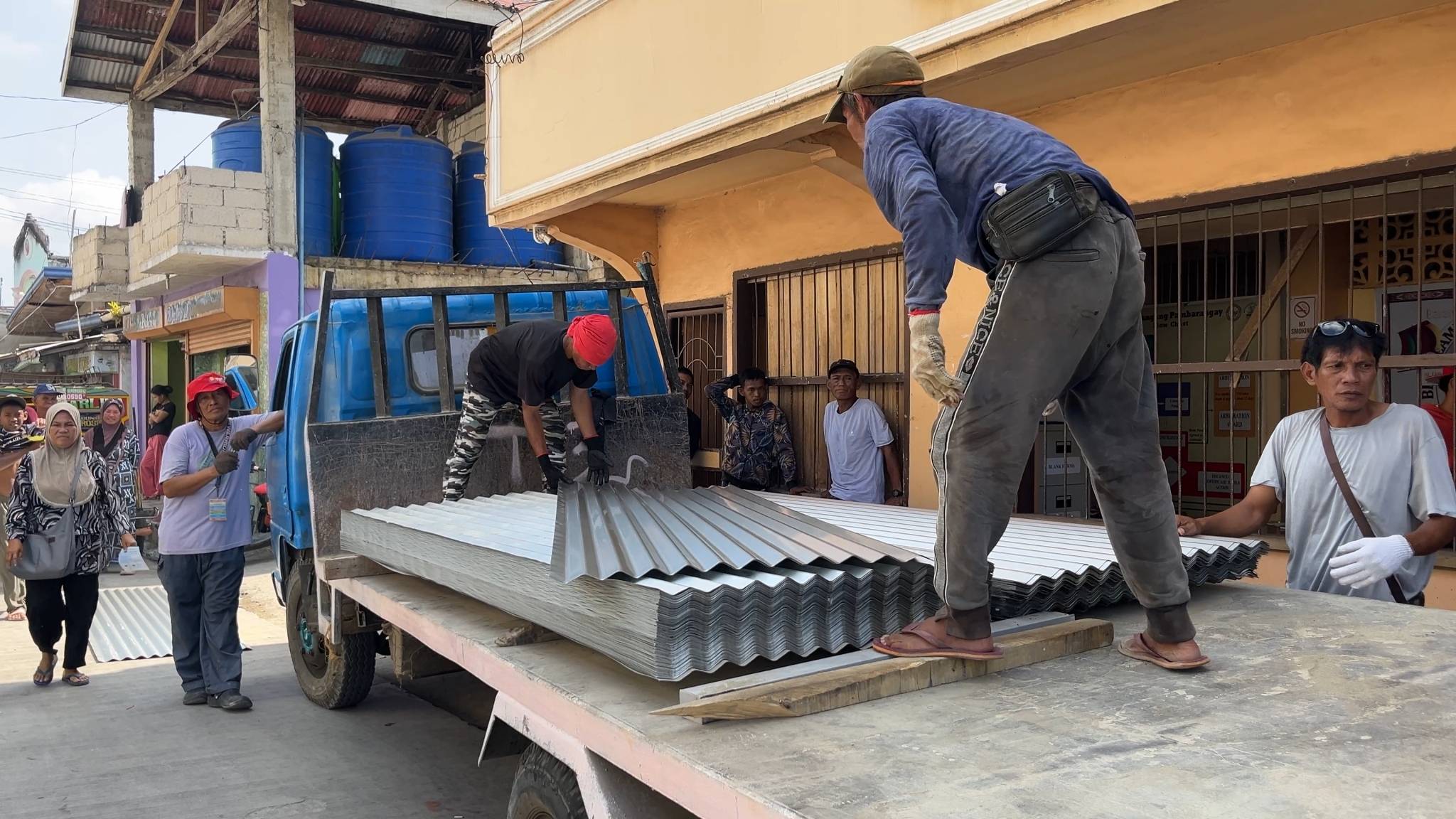 Local workers from the barangay help to unload galvanized roofing sheets. 