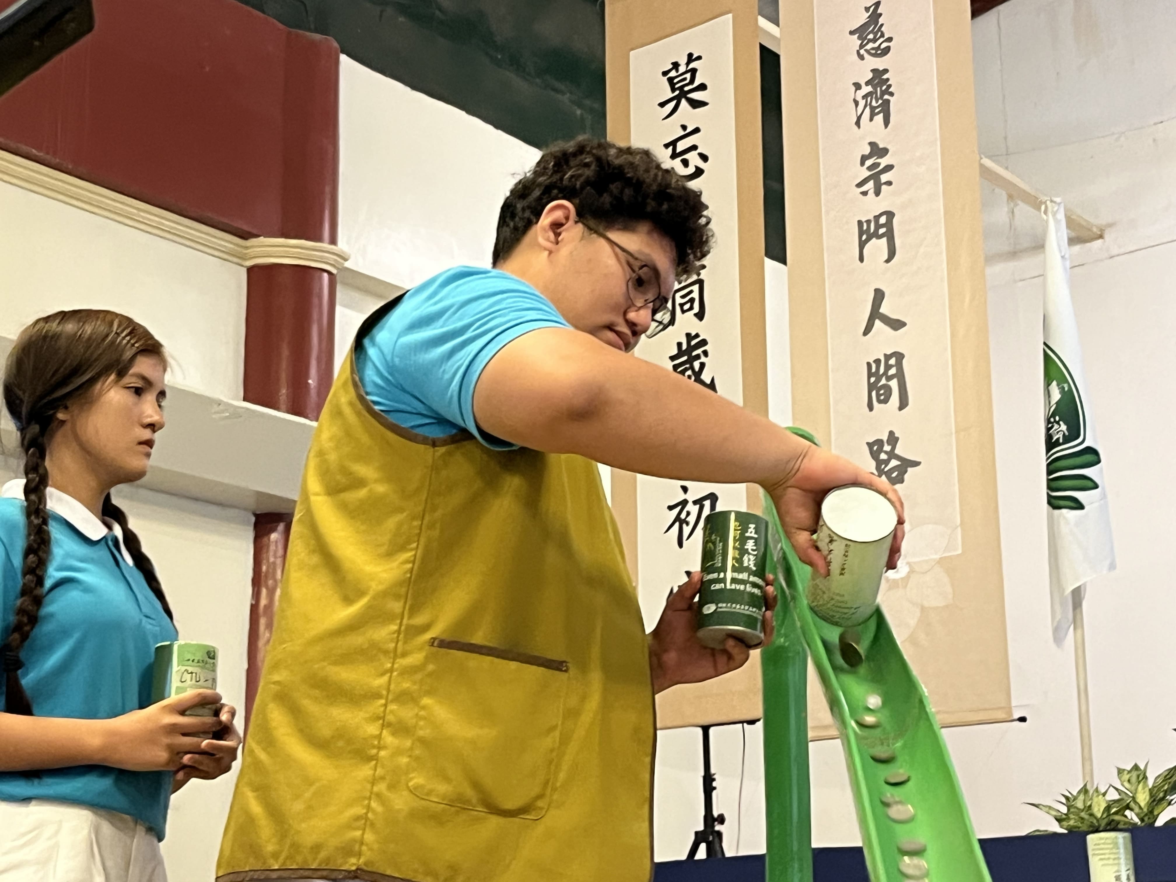 Tzu Chi Cebu scholar Andrel Arreglado pours the contents of a coin bank into a bamboo slide. “Compassion is nothing if we don't teach it to the younger generation,” he said. 