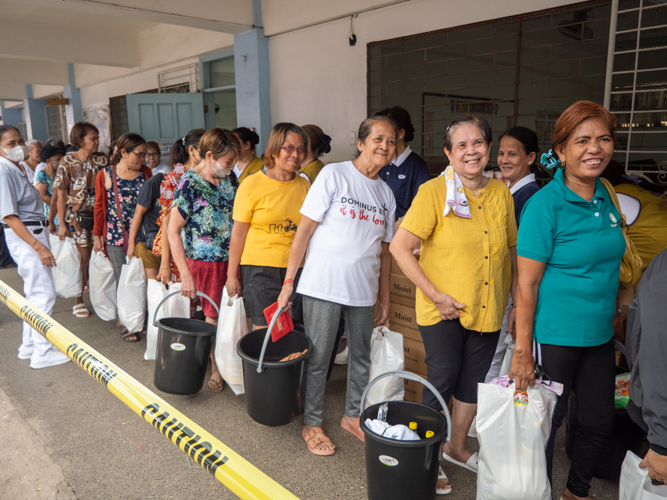 Recipients of the relief packages happily smile as they wait for their turn.