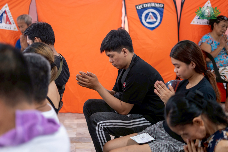 Beneficiary Alfredo Albino Jr. (in black) bows his head in prayer.