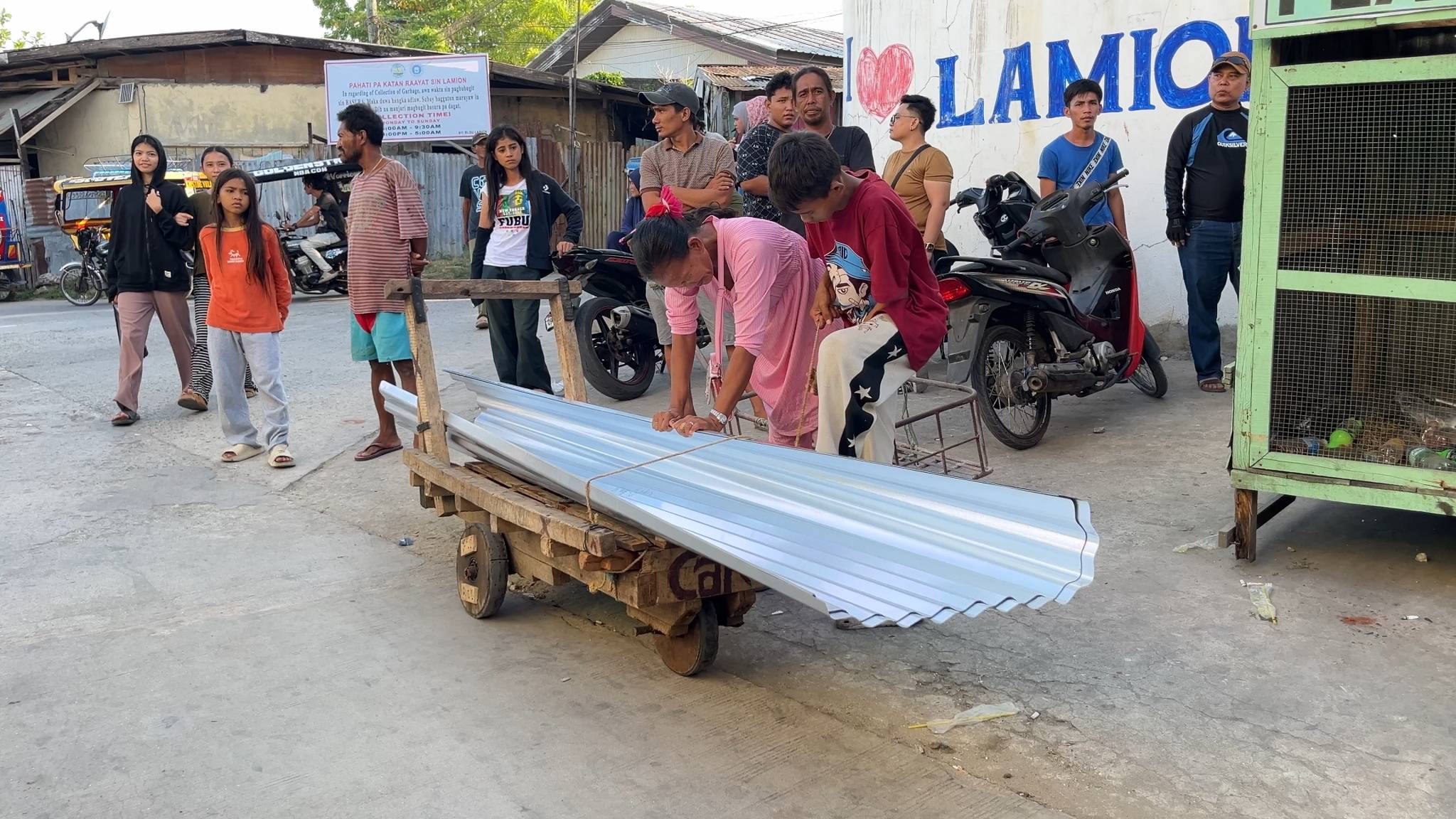 A beneficiary carefully loads her galvanized sheets onto a handcart for easier transportation to her home. 