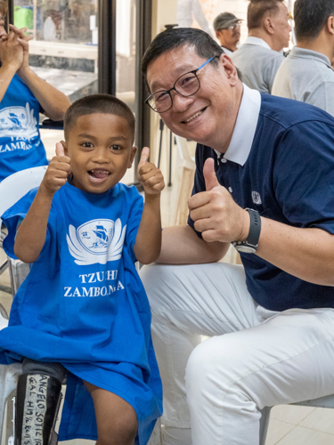 Tzu Chi Zamboanga Liaison Officer Dr. Anton Mari Lim (right) shares a thumbs-up sign with a 6-year-old prosthesis recipient, who bravely handled the process with a smile.