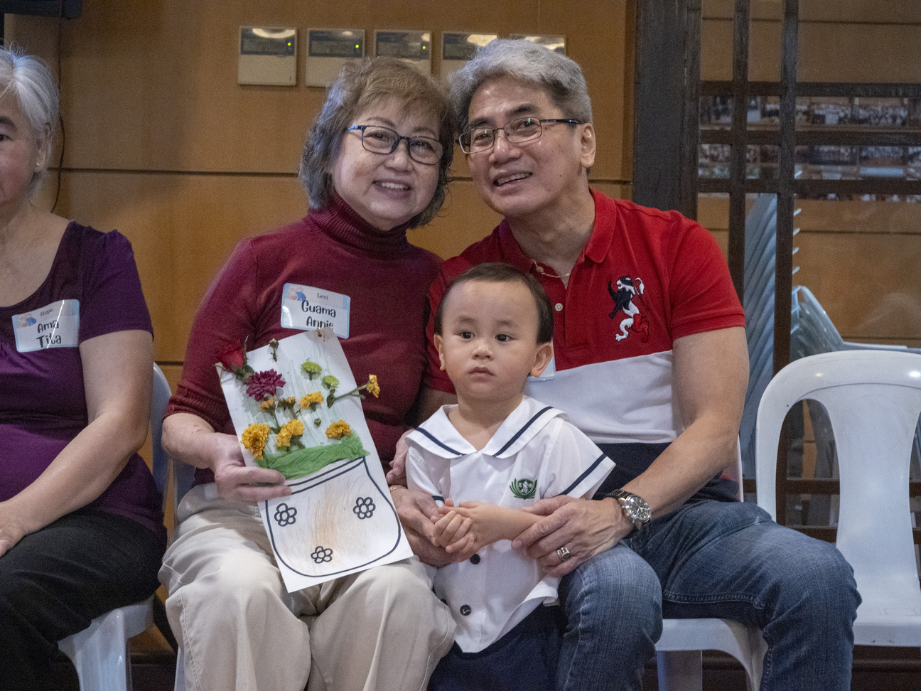 Happy grandparents pose for a photo as they receive their grandson’s handmade greeting card.