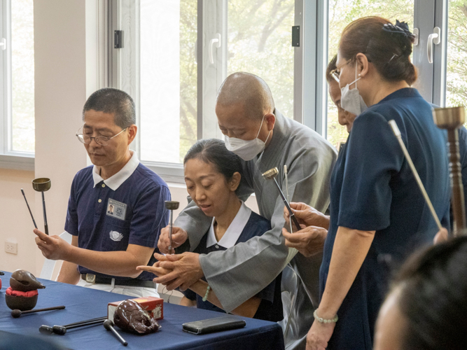 Dharma Master De Pei teaches a Tzu Chi volunteer the proper way to strike a bell.