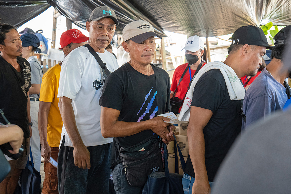 Dionisio Gorre (in black shirt with blue stripes) lines up to receive aid. He also extended assistance to his community, sharing rice and potable water donated by family members.