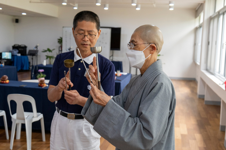 Dharma Master De Bei (right) teaches a Tzu Chi volunteer the proper way to strike a bell.