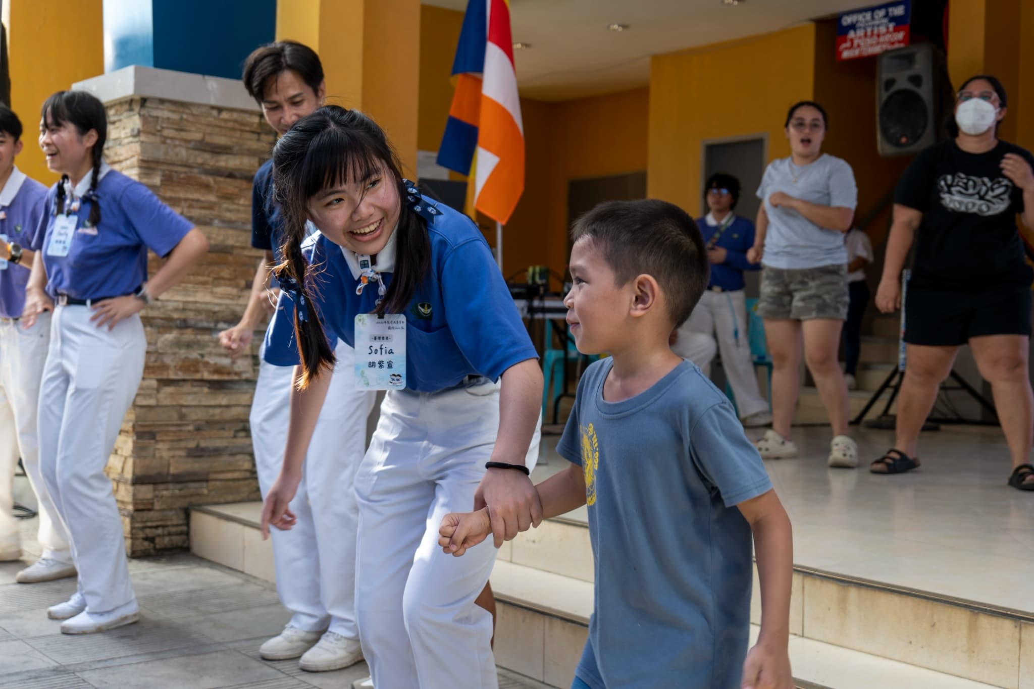 At Tzu Chi’s 292nd medical mission in Dipolog, Zamboanga del Norte, Tzu Chi Youth Sofia (Hu Zih Syuan) encourages a little boy to join their song and dance.