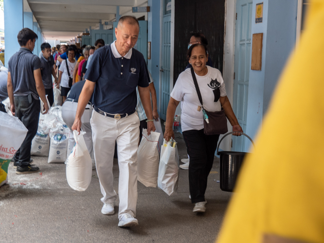 Tzu Chi volunteer Luis Diamante (left) helps a beneficiary in carrying her relief goods.