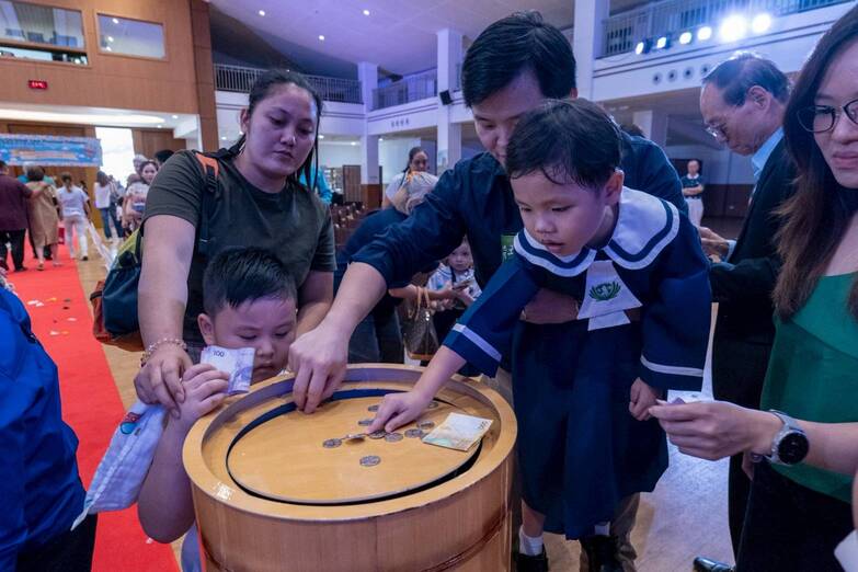 Youngsters are taught to give back by emptying the contents of their coin cans in a large wooden coin container.