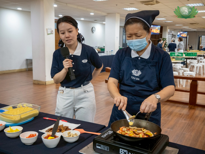 Tzu Chi volunteer Betty Dizon (left) watches as Sally Yuñez demonstrates making vegetarian pizza.