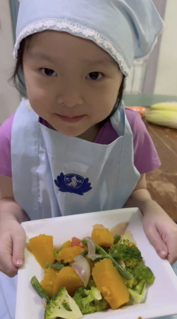 Pre-kindergarten student Harmonie proudly shows her creation: stir-fried vegetables with onions.