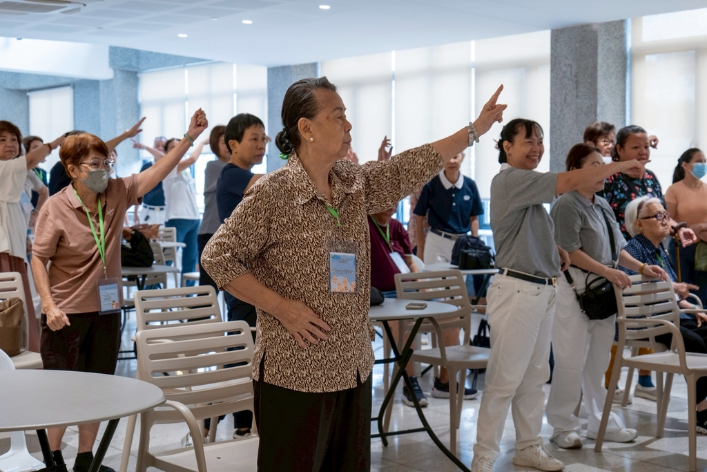 Tzu Chi volunteers and guests follow physical therapists in a seated and standing session of aerobics.