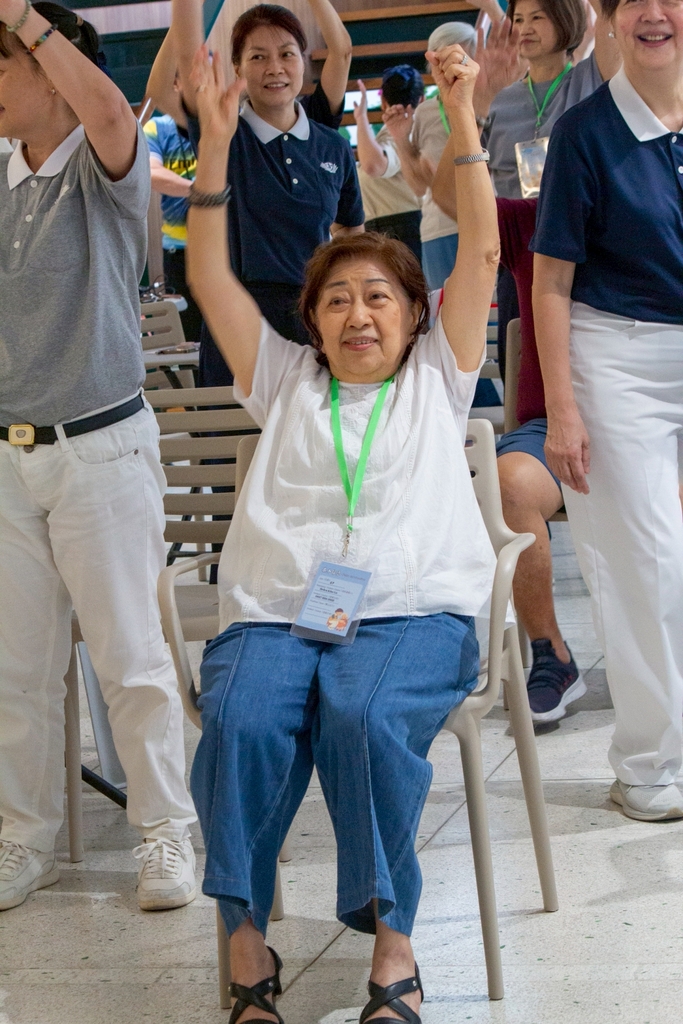Tzu Chi volunteers and guests follow physical therapists in a seated and standing session of aerobics.