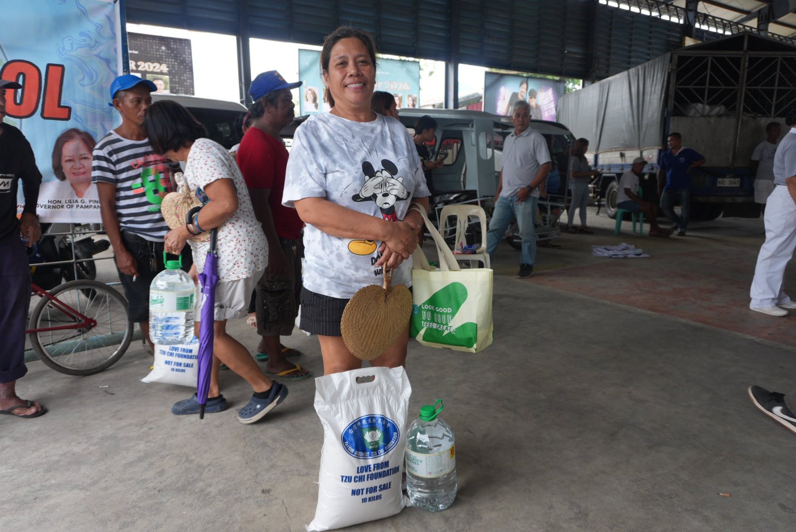 A beneficiary happily poses with her sack of rice and bottled water.