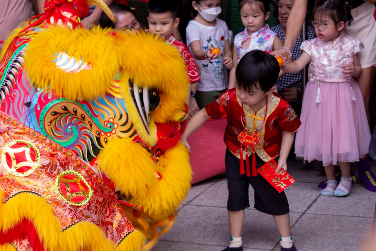 A preschooler presents a lion dancer with a fresh orange and angpao (red envelope), two symbols of luck. 