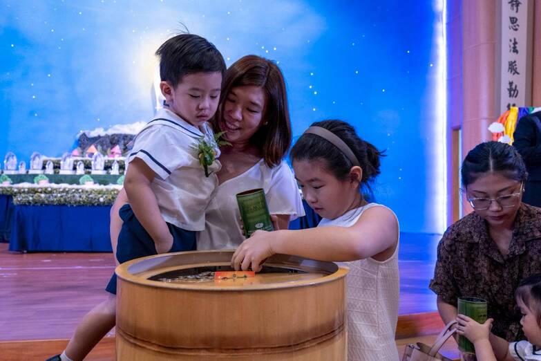 Youngsters are taught to give back by emptying the contents of their coin cans in a large wooden coin container.