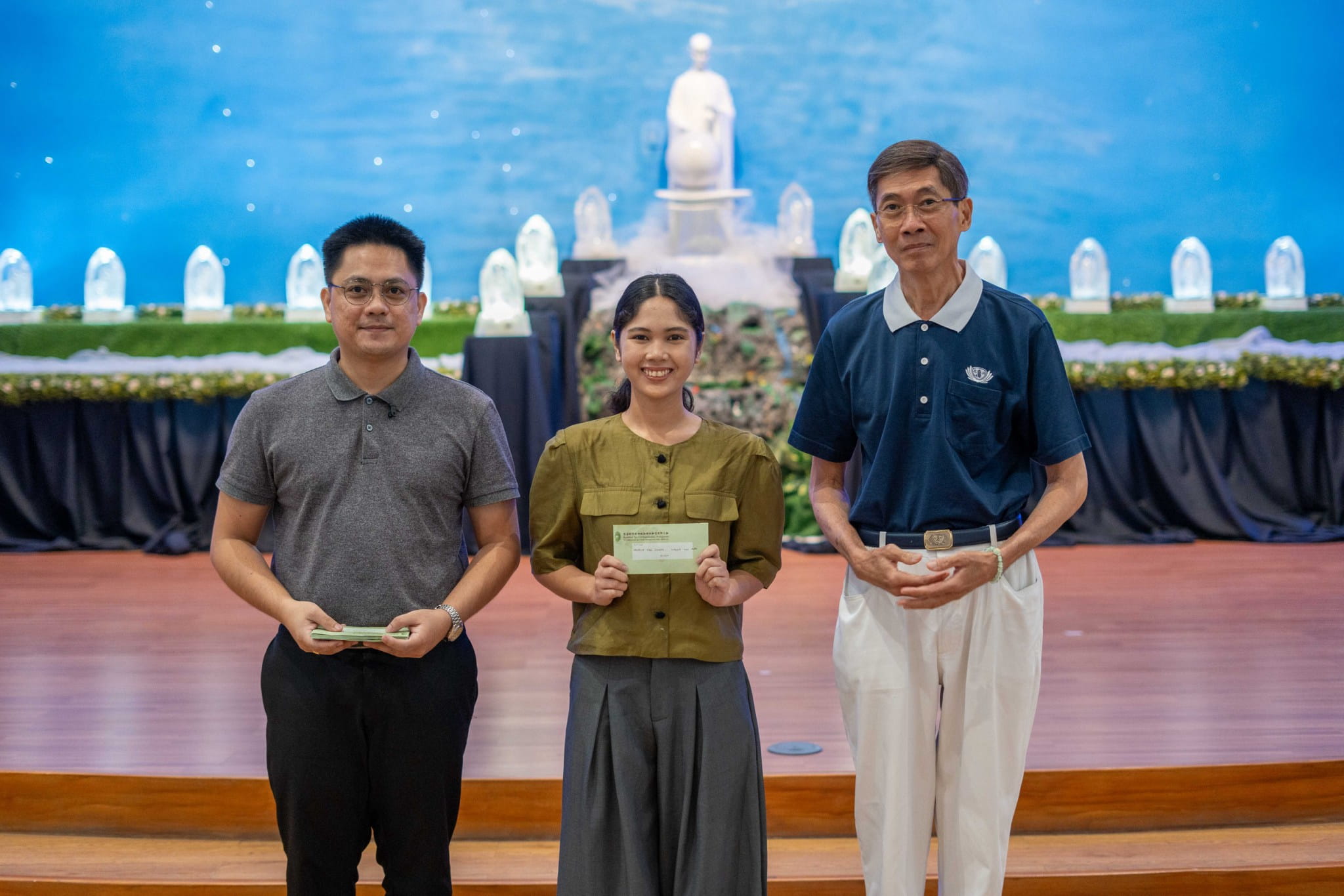 Tzu Chi scholar alumnae Daniella Dian Simran (center) uses “Tzu Chi makeup”—a big smile—when she receives her cash incentive from Tzu Chi Charity Department Head Mine Heart Tantoy (left) and Tzu Chi volunteer Johnny Cheng (right) for graduating magna cum laude.