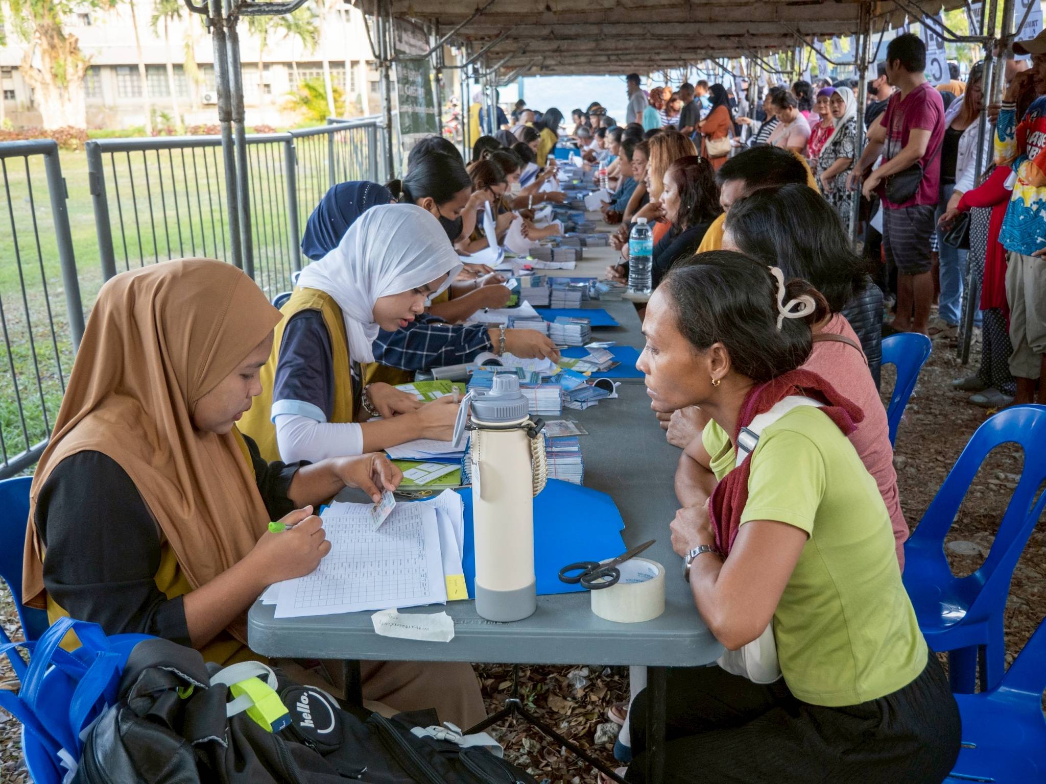 Beneficiaries gather in long lines as they wait patiently for their turn to be catered and handed out distribution stubs.