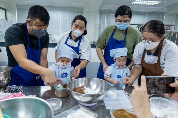 Tzu Chi Great Love Preschool Philippines Directress and volunteer Jane Sy (right) instructs students and their parents on the correct amount of dry ingredients to add.