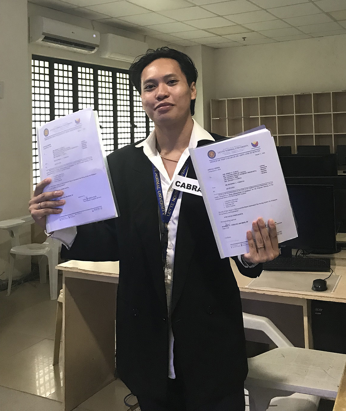 Mark Kent Cabradilla celebrates academic success, holding his  defended capstone manuscripts.