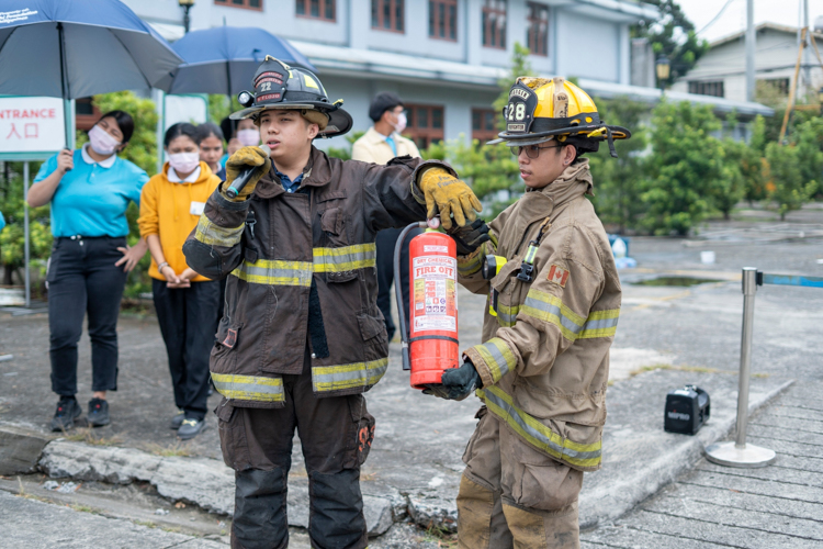 Chinatown’s volunteer firefighters teach scholars how to operate a fire extinguisher. The trick is to remember TPASS: Twist the pin to break the safety seal. Pull out the safety seal. Aim the nozzle at the base of the fire. Squeeze the lever to release the extinguishing agent. Sweep the nozzle from side to side. 