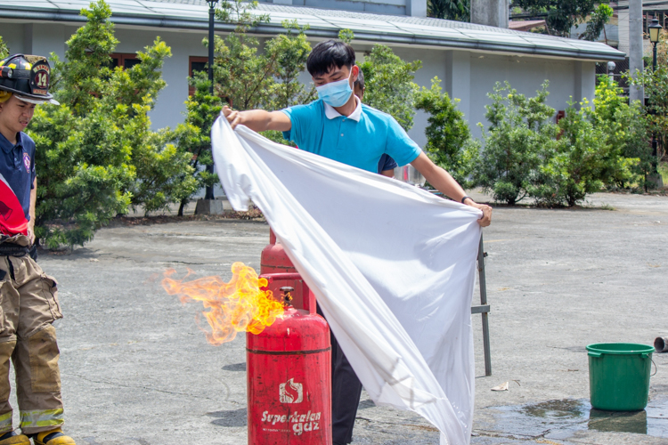Tzu Chi scholars and their parents participate in a simulated fire training exercise. Here, they use a wet blanket to extinguish fire from a gas tank. 【Photo by Marella Saldonido】